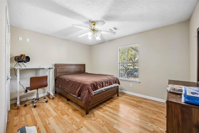 bedroom featuring a textured ceiling, ceiling fan, visible vents, baseboards, and light wood-type flooring