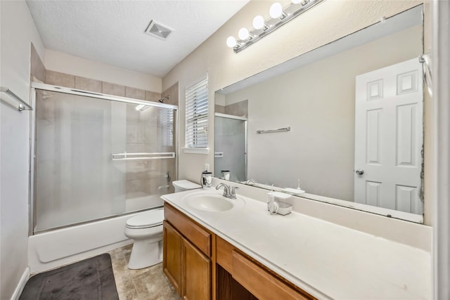 bathroom featuring visible vents, toilet, combined bath / shower with glass door, a textured ceiling, and vanity