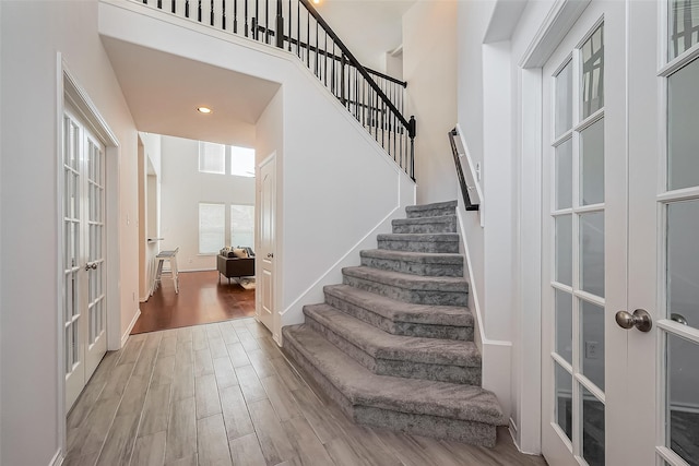 stairs with visible vents, a towering ceiling, wood finished floors, french doors, and recessed lighting