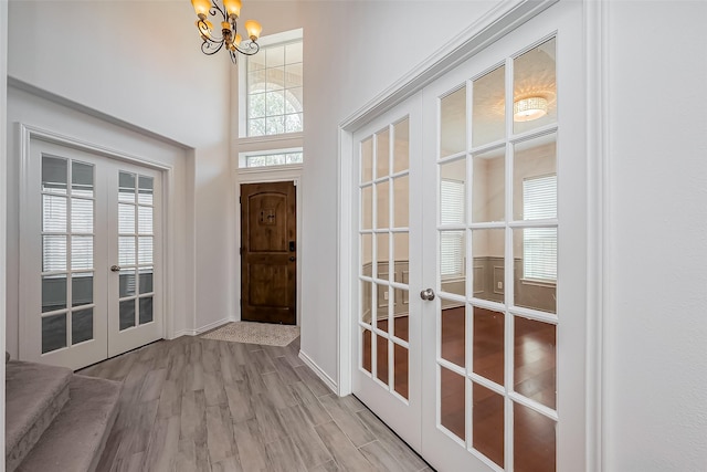 doorway to outside with a chandelier, wood finished floors, a towering ceiling, baseboards, and french doors