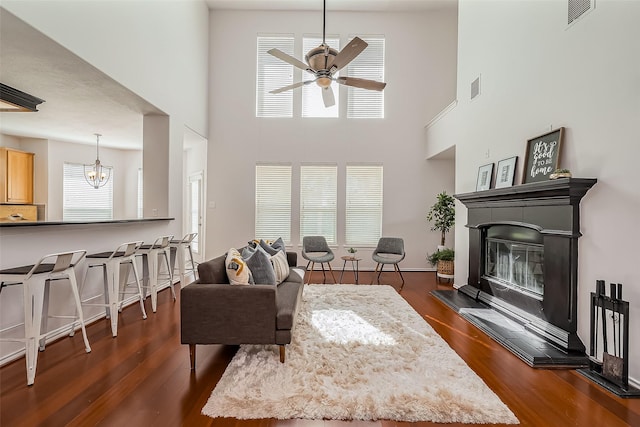 living room with ceiling fan with notable chandelier, visible vents, dark wood-type flooring, and a glass covered fireplace