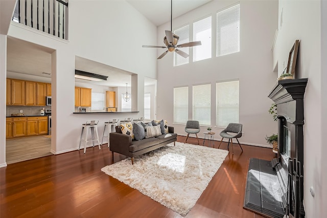 living area featuring a fireplace with flush hearth, a ceiling fan, a towering ceiling, and wood finished floors