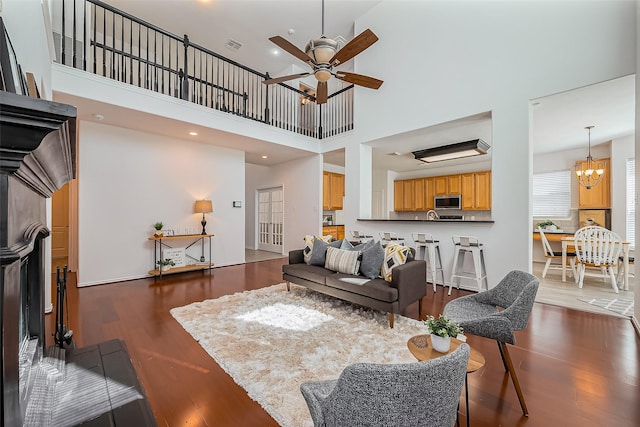 living room featuring recessed lighting, ceiling fan with notable chandelier, wood finished floors, a towering ceiling, and visible vents