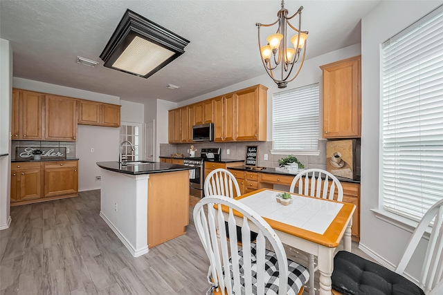 kitchen with a sink, appliances with stainless steel finishes, backsplash, dark countertops, and an inviting chandelier