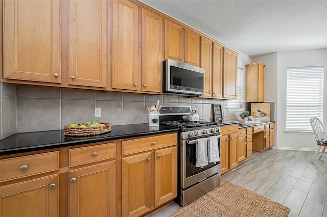 kitchen featuring a textured ceiling, baseboards, appliances with stainless steel finishes, tasteful backsplash, and dark countertops