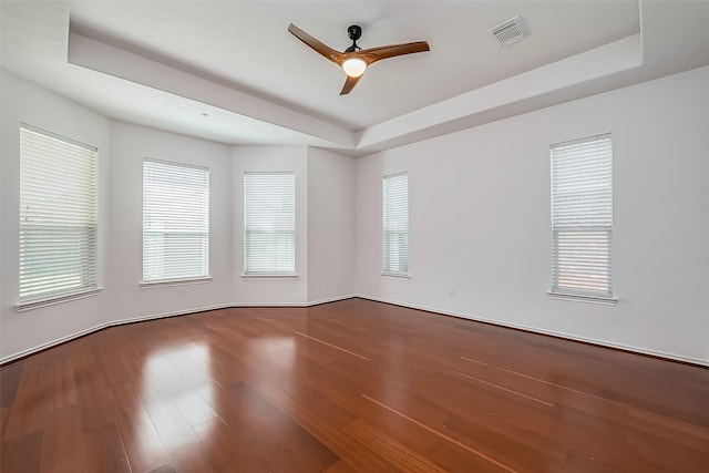 spare room with a ceiling fan, a tray ceiling, visible vents, and wood finished floors