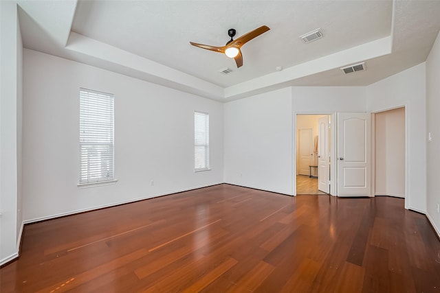 unfurnished bedroom with a tray ceiling, visible vents, and wood finished floors