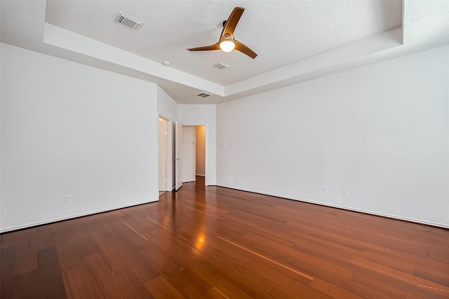 spare room with a ceiling fan, visible vents, a tray ceiling, and wood finished floors