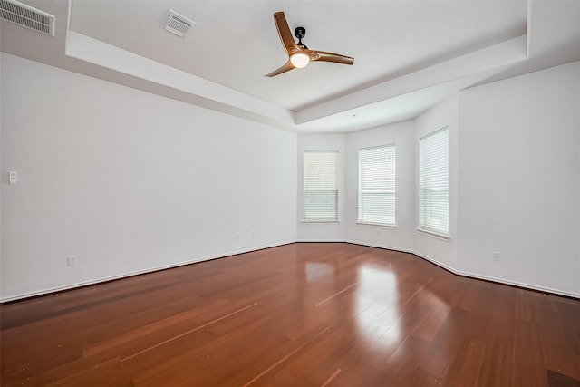 unfurnished room featuring a tray ceiling, visible vents, ceiling fan, and wood finished floors