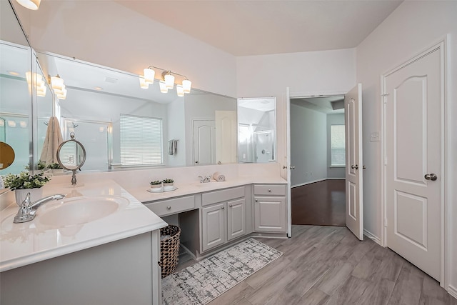 bathroom featuring double vanity, a sink, a shower stall, and wood finished floors