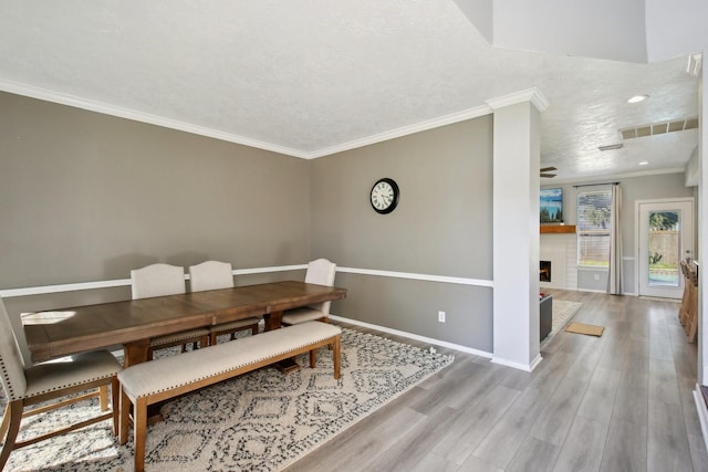 dining space with baseboards, visible vents, wood finished floors, crown molding, and a fireplace