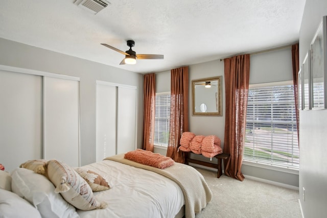 bedroom with ceiling fan, a textured ceiling, light carpet, visible vents, and multiple closets