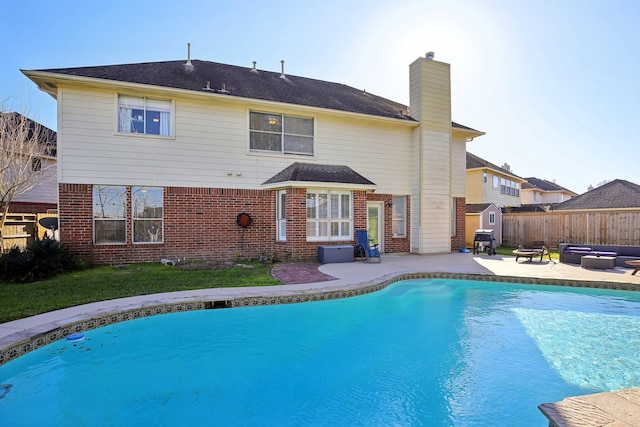 back of house with brick siding, a chimney, outdoor lounge area, a patio area, and fence