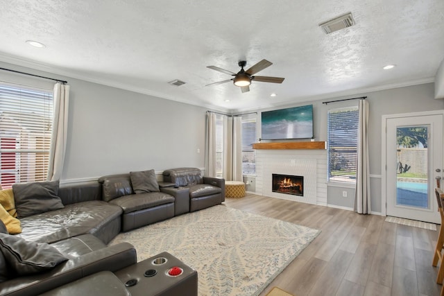 living area with a warm lit fireplace, visible vents, crown molding, and wood finished floors