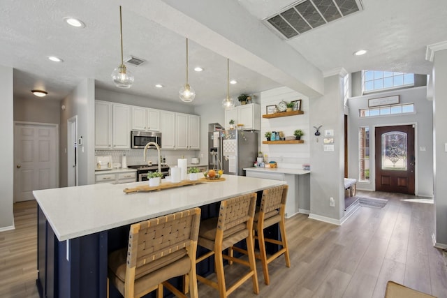 kitchen featuring stainless steel appliances, light wood-type flooring, visible vents, and decorative backsplash