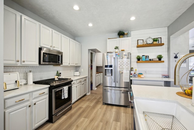 kitchen featuring open shelves, backsplash, appliances with stainless steel finishes, light wood-style floors, and a sink