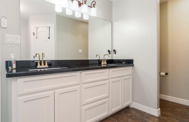 full bath with double vanity, a sink, baseboards, and wood finished floors