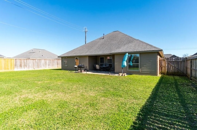 back of property with a shingled roof, a patio area, a fenced backyard, and a lawn