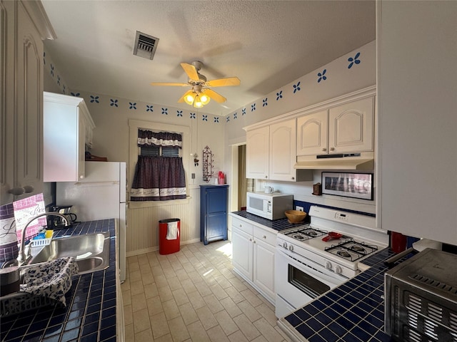 kitchen with tile countertops, white cabinetry, a sink, white appliances, and under cabinet range hood