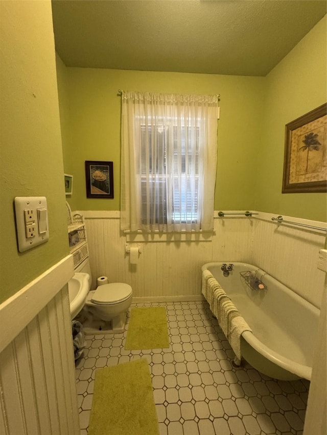 full bath featuring wainscoting, a freestanding bath, toilet, and tile patterned floors