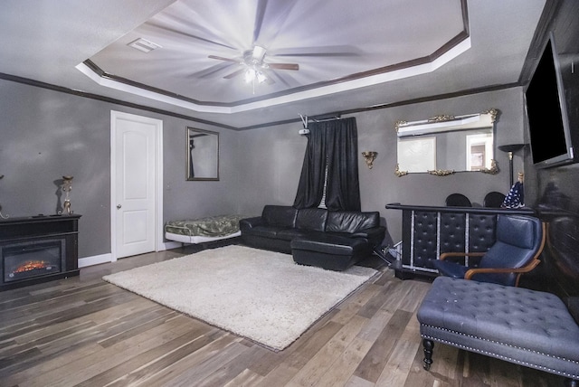 living room featuring a tray ceiling, crown molding, visible vents, a glass covered fireplace, and wood finished floors