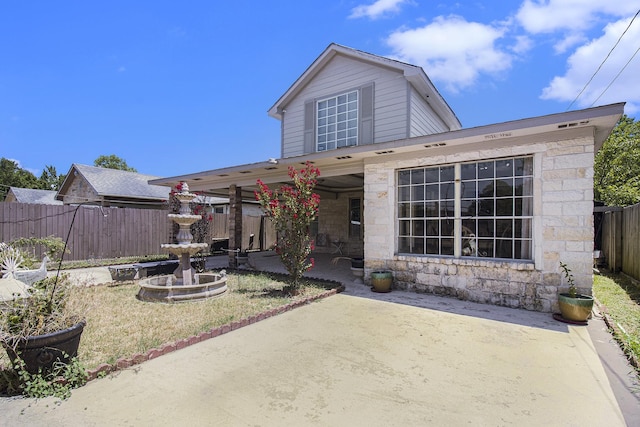 rear view of house with stone siding, a patio area, and fence