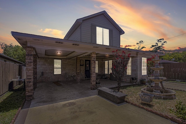 view of front of property with a patio area, stone siding, and fence