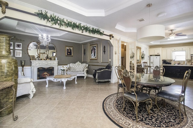 dining space with a warm lit fireplace, light tile patterned floors, visible vents, ornamental molding, and a raised ceiling