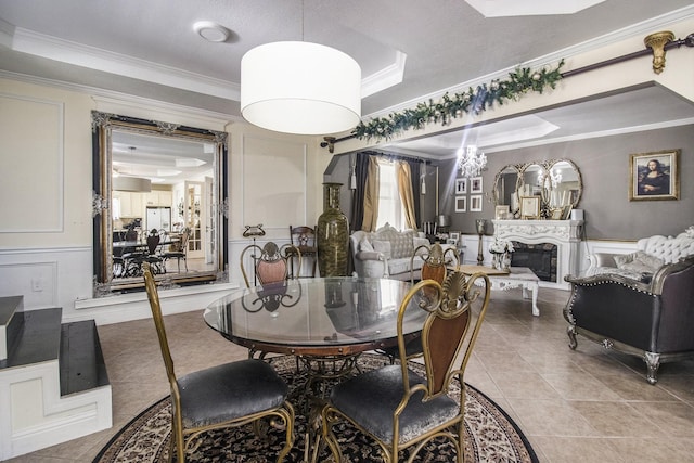 dining room featuring tile patterned flooring, a decorative wall, a tray ceiling, a glass covered fireplace, and crown molding