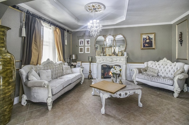 tiled living area featuring a raised ceiling, a decorative wall, ornamental molding, a chandelier, and a warm lit fireplace