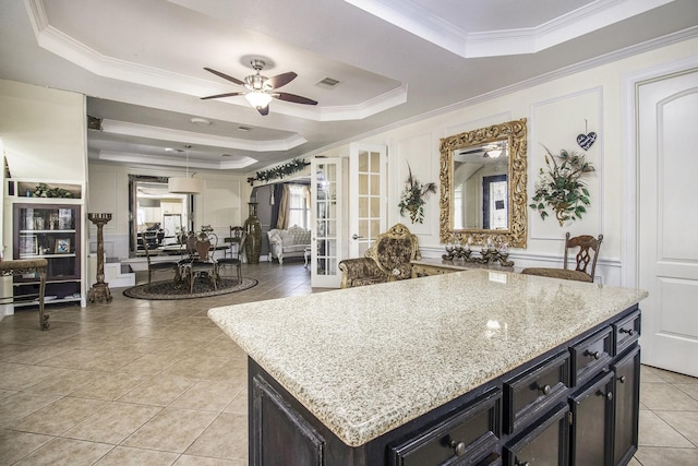 kitchen with light tile patterned floors, visible vents, light stone countertops, a tray ceiling, and crown molding