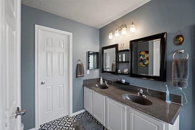 full bathroom featuring double vanity, a textured ceiling, baseboards, and a sink