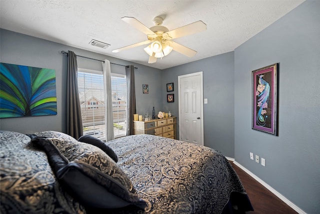 bedroom with a textured ceiling, dark wood-type flooring, a ceiling fan, visible vents, and baseboards