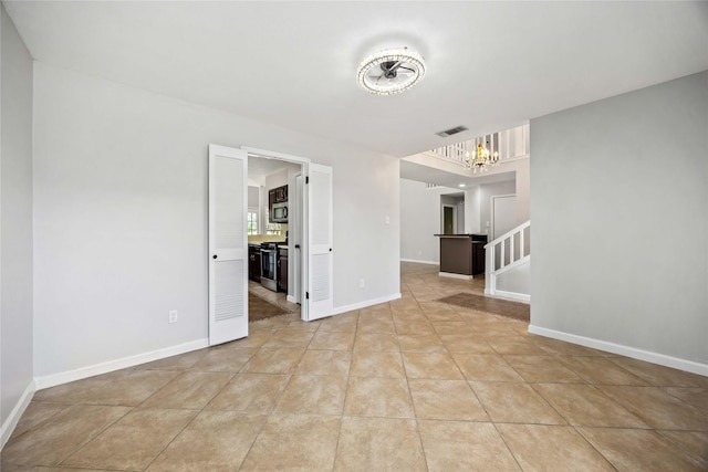 empty room with light tile patterned floors, visible vents, a chandelier, baseboards, and stairs