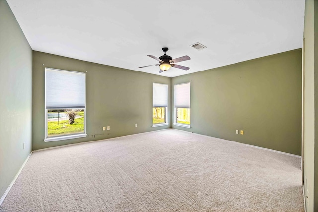 carpeted spare room featuring a ceiling fan, a wealth of natural light, visible vents, and baseboards