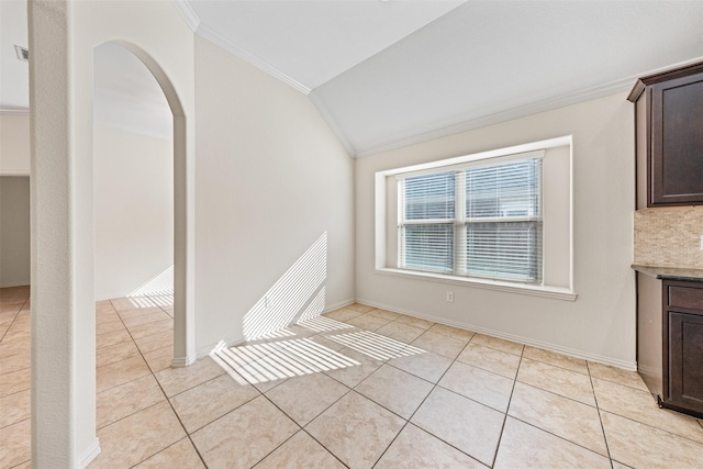 unfurnished dining area with light tile patterned floors, arched walkways, lofted ceiling, baseboards, and crown molding