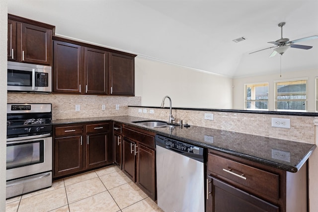 kitchen with dark brown cabinetry, dark stone counters, appliances with stainless steel finishes, a peninsula, and a sink