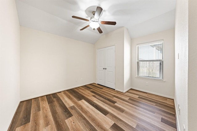 unfurnished bedroom with lofted ceiling, wood finished floors, a ceiling fan, baseboards, and a closet