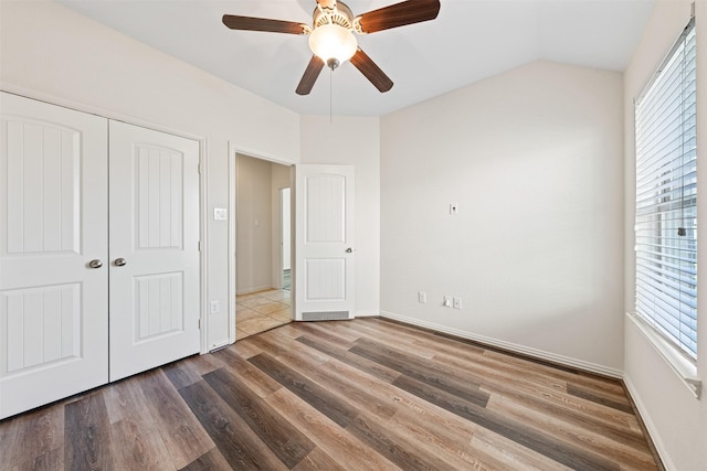 unfurnished bedroom featuring baseboards, lofted ceiling, ceiling fan, wood finished floors, and a closet