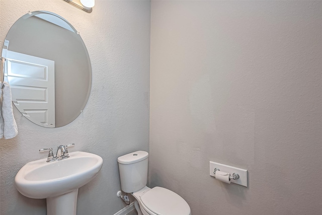 bathroom featuring toilet, a textured wall, and a sink