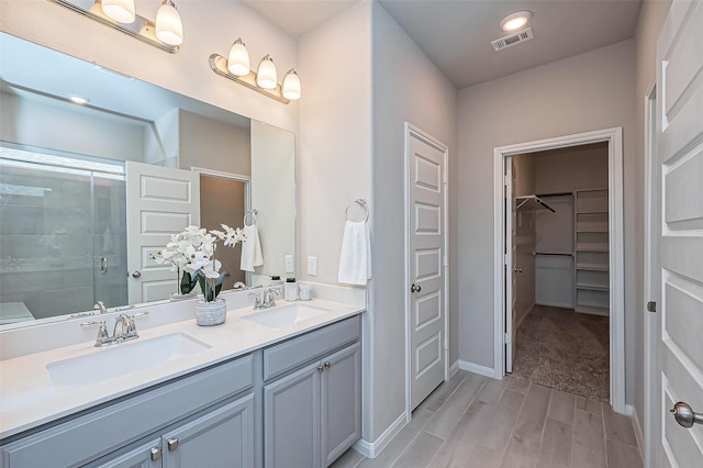 full bath featuring a sink, visible vents, wood finished floors, and a shower stall