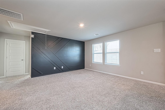 carpeted empty room featuring visible vents, baseboards, and attic access