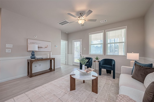 living room featuring visible vents, baseboards, light wood-style floors, and a ceiling fan