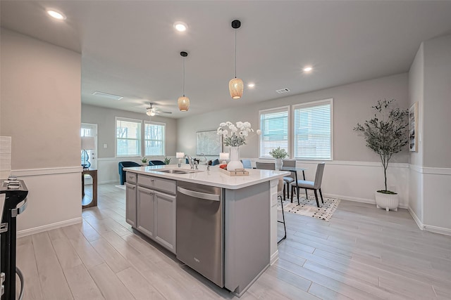 kitchen with light wood-type flooring, a center island with sink, a sink, stainless steel dishwasher, and light countertops