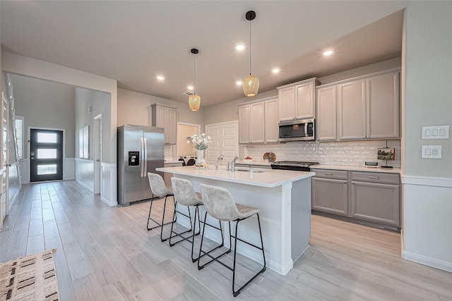 kitchen with light wood finished floors, gray cabinets, a sink, stainless steel appliances, and a kitchen breakfast bar