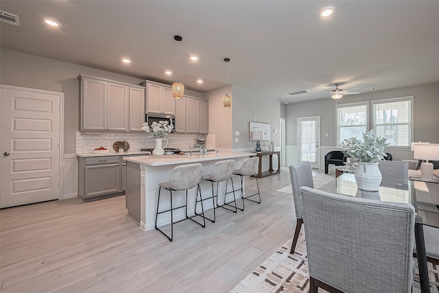 kitchen featuring light wood-type flooring, a kitchen bar, gray cabinets, stainless steel microwave, and open floor plan