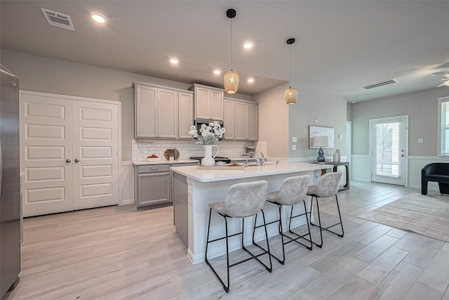 kitchen with light wood finished floors, visible vents, gray cabinets, and a kitchen breakfast bar