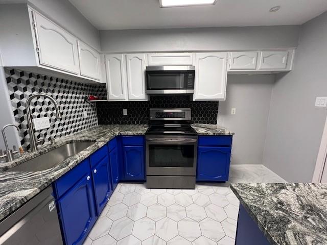 kitchen featuring stainless steel appliances, white cabinets, a sink, and blue cabinetry