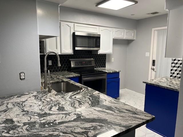 kitchen with appliances with stainless steel finishes, stone counters, a sink, and white cabinetry