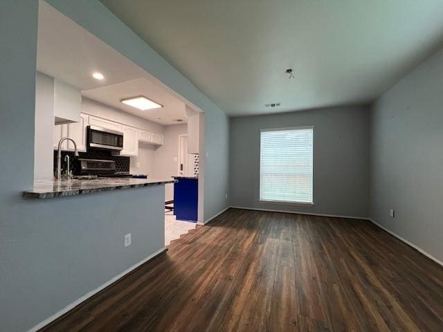 kitchen featuring a peninsula, white cabinetry, tasteful backsplash, stainless steel microwave, and dark wood finished floors